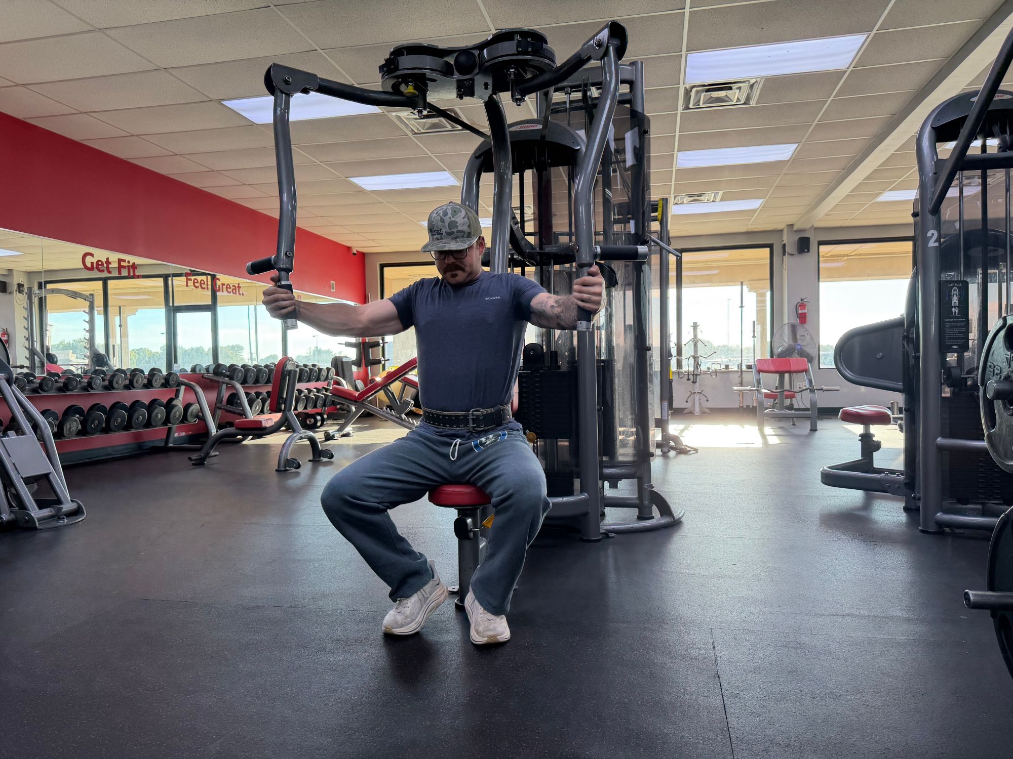 A member training on the pec deck by the dumbbell racks